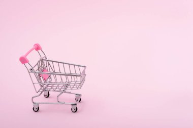 Açık pembe arka planda tekerlekleri olan boş mini metal alışveriş arabası ve metin için fotokopi alanı. Süpermarkette konsept alışverişi.