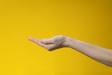 Sarı arka planda bir kadının el hareketi. Sorma veya verme jesti.