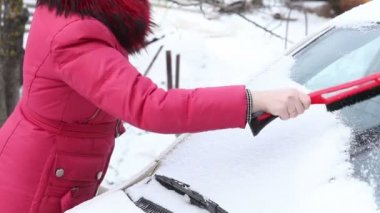 kadın kırmızı ceketli bir araba penceresinden kar temizlemek için.