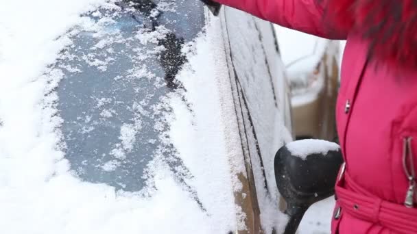 Vrouw in een rood jasje om duidelijk van sneeuw van de autoruit. — Stockvideo