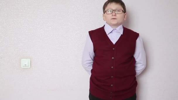 Niño con gafas de pie contra una pared y mirando a la cámara — Vídeos de Stock