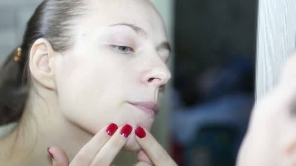 Mujer aprieta espinillas en su cara mirando en un espejo — Vídeo de stock