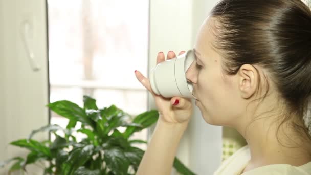 Giovane ragazza che guarda fuori dalla finestra bere caffè — Video Stock