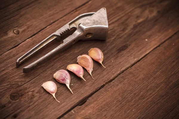 Mačkadlo na česneku a česnek na dřevěné pozadí — Stock fotografie