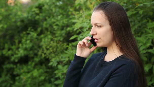 Menina bonita falando ao telefone no parque entre as árvores — Vídeo de Stock