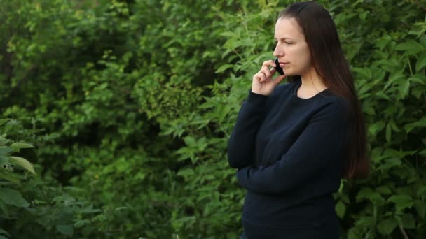 Красивая девушка разговаривает по телефону в парке среди деревьев — стоковое видео