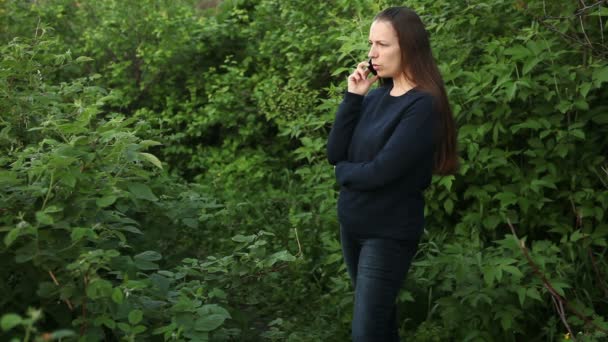 Güzel kız parkta ağaçların arasında telefonda konuşuyor — Stok video