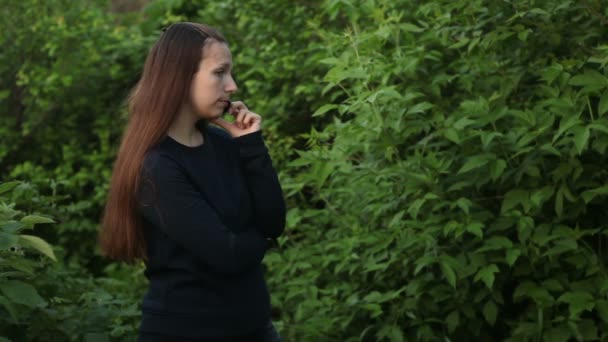 Menina bonita falando ao telefone no parque entre as árvores — Vídeo de Stock