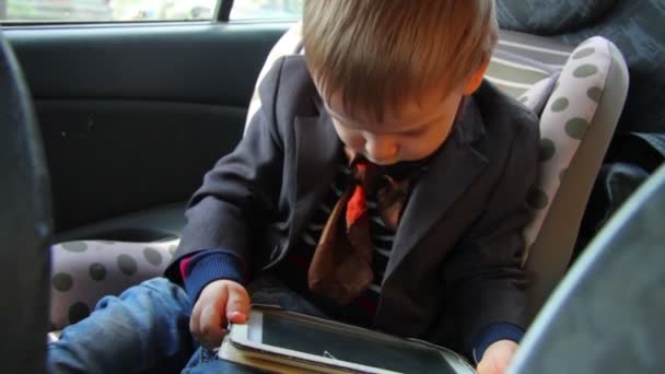 Malý chlapec v tabletu, sedí v autě autosedačku — Stock video