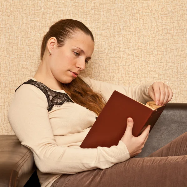 Mladá dívka sedí na gauči a čtení knihy — Stock fotografie