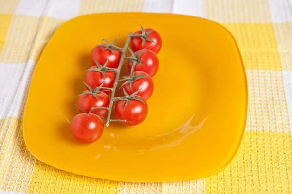Cherry tomatoes on a branch on a yellow plate — Stock Photo, Image