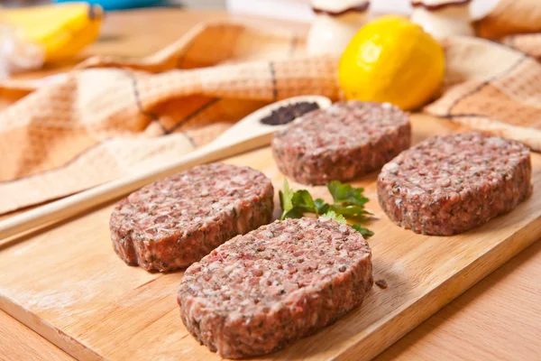 Raw burgers on a cutting board with lemon wedges — Stock Photo, Image