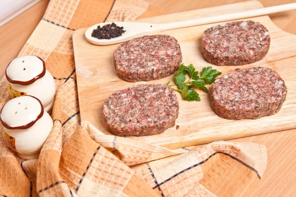 Raw burgers on a cutting board with lemon wedges — Stock Photo, Image