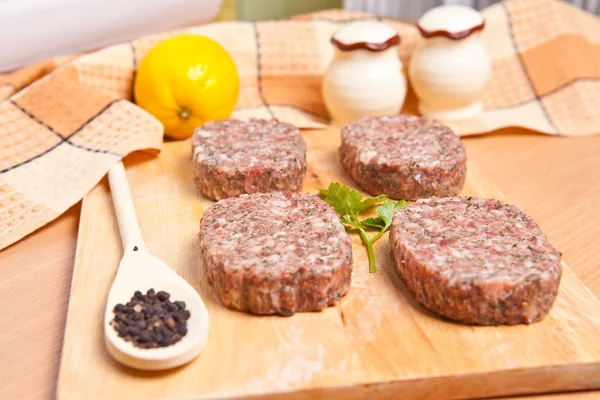 Raw burgers on a cutting board with lemon wedges — Stock Photo, Image