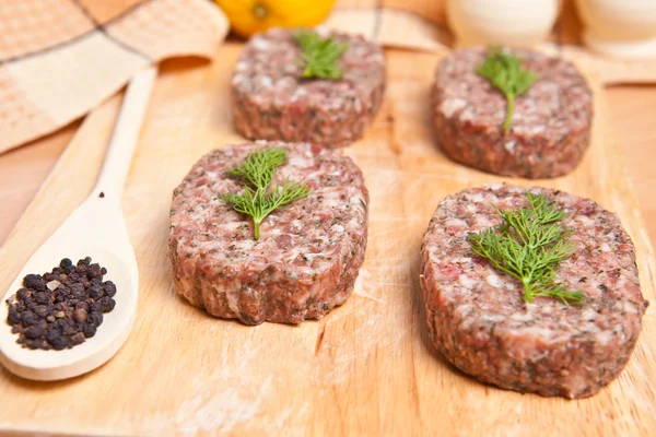 Raw burgers on a cutting board with lemon wedges — Stock Photo, Image