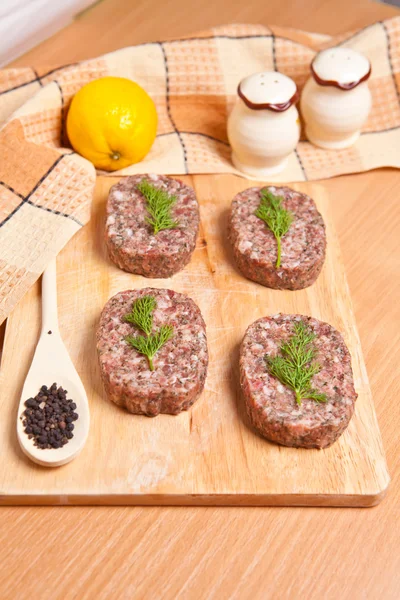 Raw burgers on a cutting board with lemon wedges — Stock Photo, Image