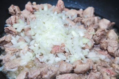 bir tavada kızarmış soğanlı et parçaları