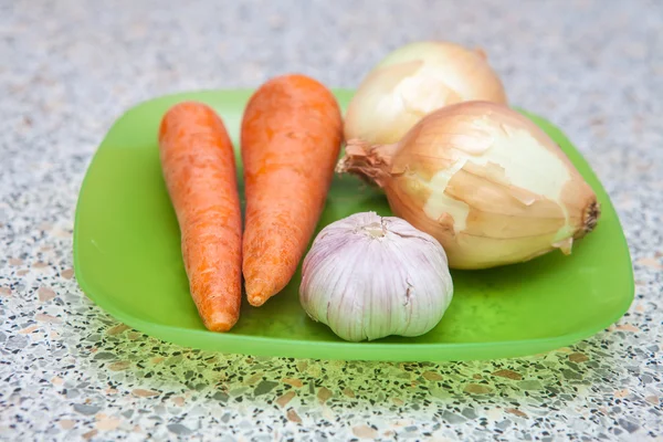 Cebollas crudas zanahorias y ajo en un plato de plástico sobre la mesa —  Fotos de Stock