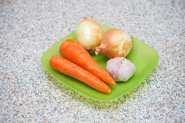 Cebollas crudas zanahorias y ajo en un plato de plástico sobre la mesa —  Fotos de Stock