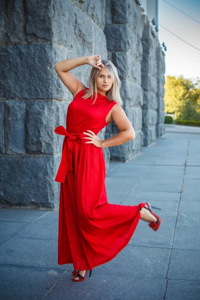 Mooi meisje poseren in een rode jurk van de avond in het park buiten — Stockfoto