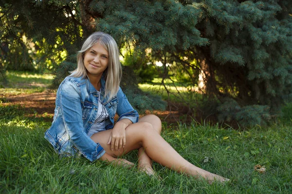 Poseren mooi meisje, zittend op het grasveld in het park; buitenshuis. — Stockfoto