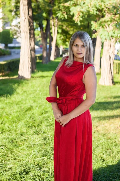Όμορφη κοπέλα ποζάρει σε ένα κόκκινο φόρεμα βράδυ στο υπαίθριο πάρκο — Φωτογραφία Αρχείου