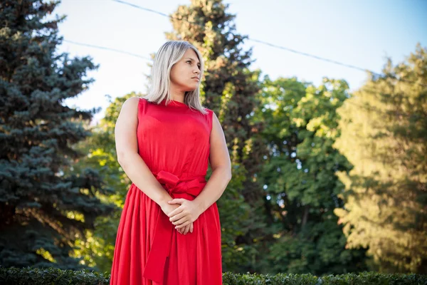 야외 공원에 빨간 이브닝 드레스에 포즈를 취하는 아름 다운 소녀 — 스톡 사진