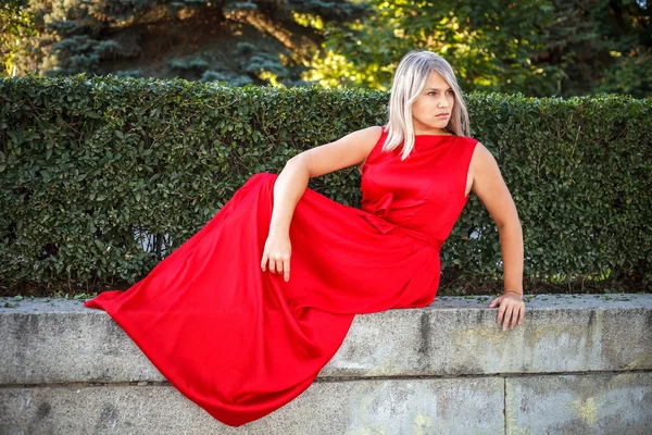 Красивая девушка позирует в красном вечернем платье в парке на открытом воздухе — стоковое фото