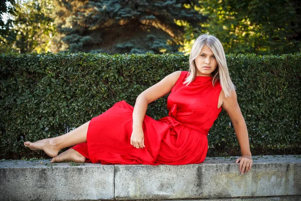 Schöne Mädchen posiert in einem roten Abendkleid im Park draußen — Stockfoto