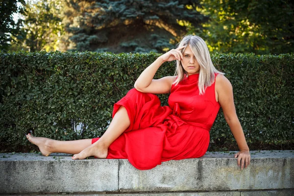 Beautiful girl posing in a red evening dress in the park outdoor — Stock Photo, Image