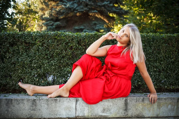 Beautiful girl posing in a red evening dress in the park outdoor — Stock Photo, Image