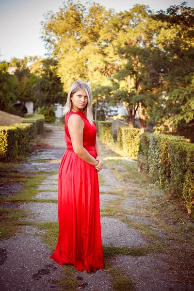 Mooi meisje poseren in een rode jurk van de avond in het park buiten — Stockfoto