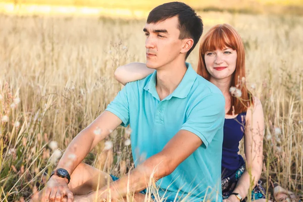 Young couple sitting side by side in the field, outdoors — Stock Photo, Image