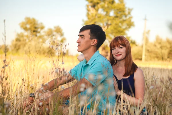 Young couple sitting side by side in the field, outdoors — Stock Photo, Image