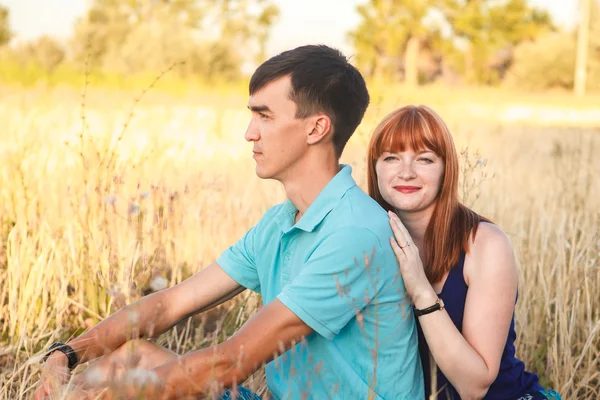Young couple sitting side by side in the field, outdoors — Stock Photo, Image