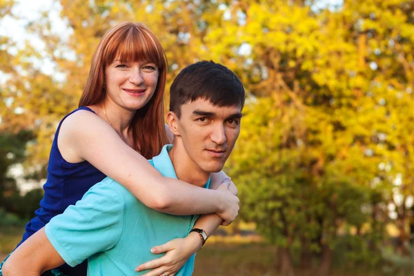 Girl sitting on the back of a guy walk in the park outdoors — Stock Photo, Image