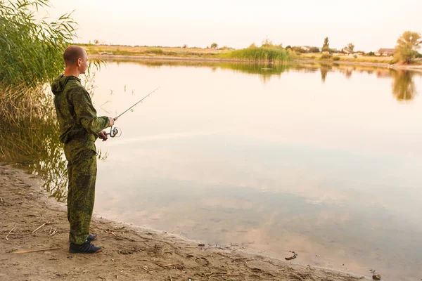 Hombre en traje de camuflaje es la pesca en el estanque — Foto de Stock