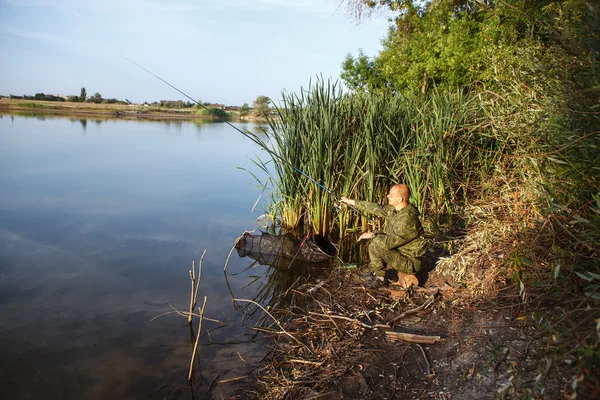 Man in camouflage suit is fishing on the pond — Stock Photo, Image