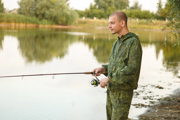 Man in camouflage suit is fishing on the pond — Stock Photo, Image