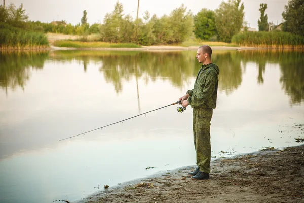 Man in camouflage suit is fishing on the pond — Stock Photo, Image