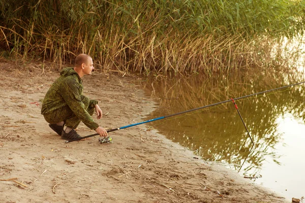 Homme en costume de camouflage pêche sur l'étang — Photo