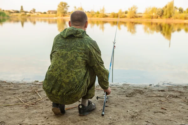 Fisherman sitting in front of a fishing rod on the shore of the — Stock Photo, Image