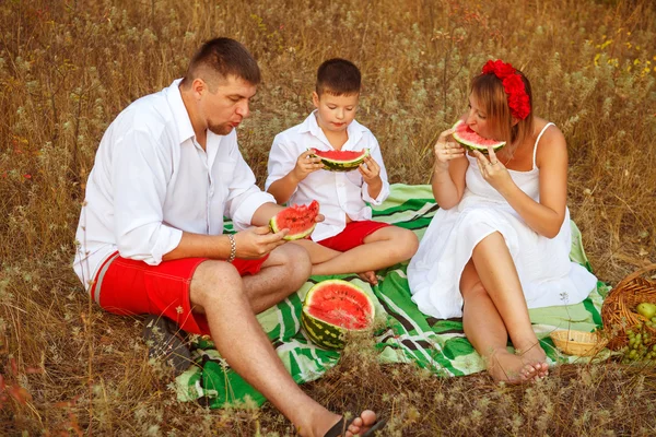 Família de três comendo melancia sentado em um tapete na floresta — Fotografia de Stock