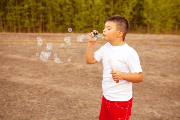 Pojken blåser såpbubblor i parken utomhus — Stockfoto