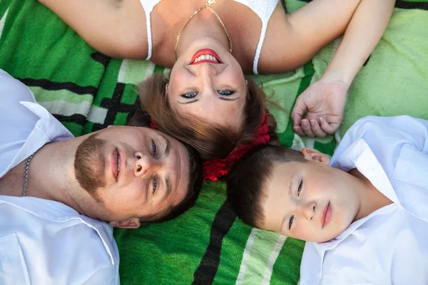 Moeder, vader en zoon liggen op het tapijt hoofd tot hoofd bovenaanzicht — Stockfoto