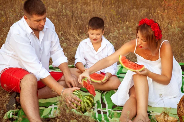 Família de três comendo melancia sentado em um tapete na floresta — Fotografia de Stock