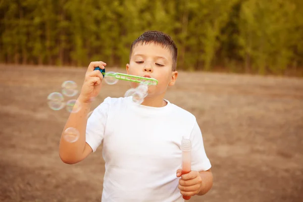 屋外の公園でシャボン玉を吹く少年 — ストック写真