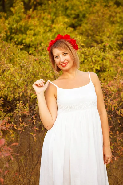 Hermosa mujer con una corona de flores rojas en un campo al aire libre —  Fotos de Stock