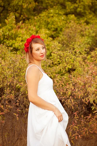 Hermosa mujer con una corona de flores rojas en un campo al aire libre —  Fotos de Stock