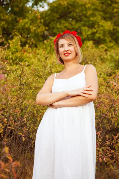 Hermosa mujer con una corona de flores rojas en un campo al aire libre —  Fotos de Stock